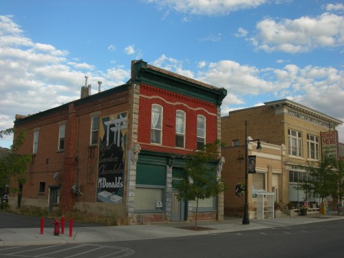 Historic buildings with a McDonald's sign, under a blue sky with clouds, in a small town setting.