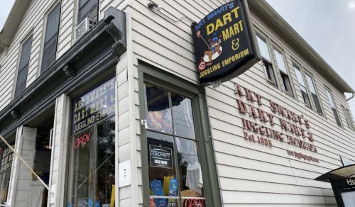 Exterior of Art Smith's Dart Mart & Juggling Emporium, featuring a sign and an open door, with a classic building style.