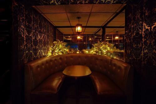Cozy booth in a dimly lit bar, adorned with plants and warm string lights, creating an inviting atmosphere.