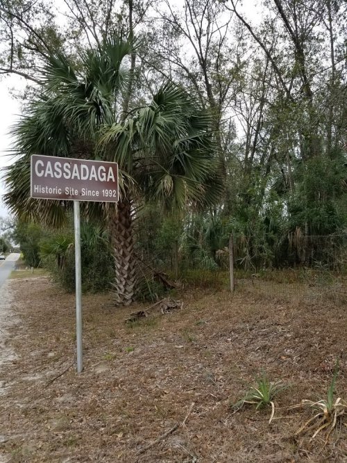 Sign for Cassadaga, a historic site since 1992, surrounded by trees and palm plants.