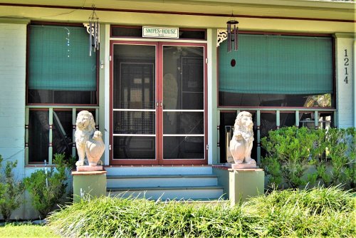 Front entrance of a house with green window shades, two lion statues, and a sign reading "Snoopy's House."