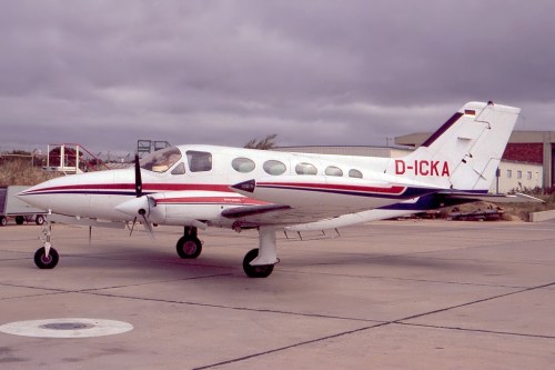 A small twin-engine aircraft on a tarmac, with a red and white design and the registration D-ICKA.