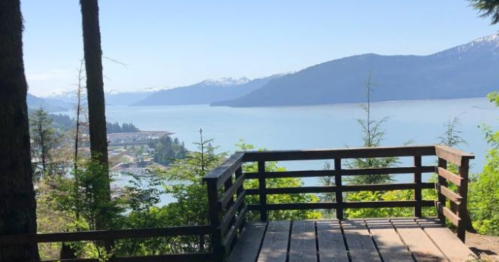 Scenic view from a wooden overlook, featuring a lake surrounded by mountains and lush greenery.