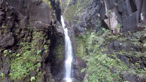A serene waterfall cascading down rocky cliffs, surrounded by lush green vegetation.