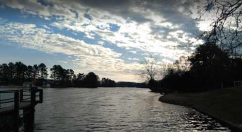 A serene river scene with a cloudy sky, trees lining the shore, and a wooden dock extending into the water.