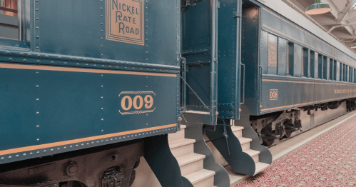 Two vintage train cars from the Nickel Plate Road, featuring blue exteriors and decorative details, displayed indoors.