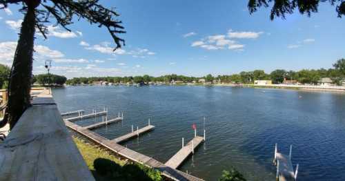 A serene lake view with docks, surrounded by trees and blue skies dotted with clouds.