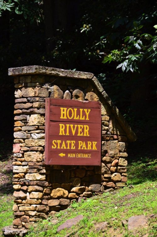 Sign for Holly River State Park at the main entrance, featuring stone structure and yellow lettering.