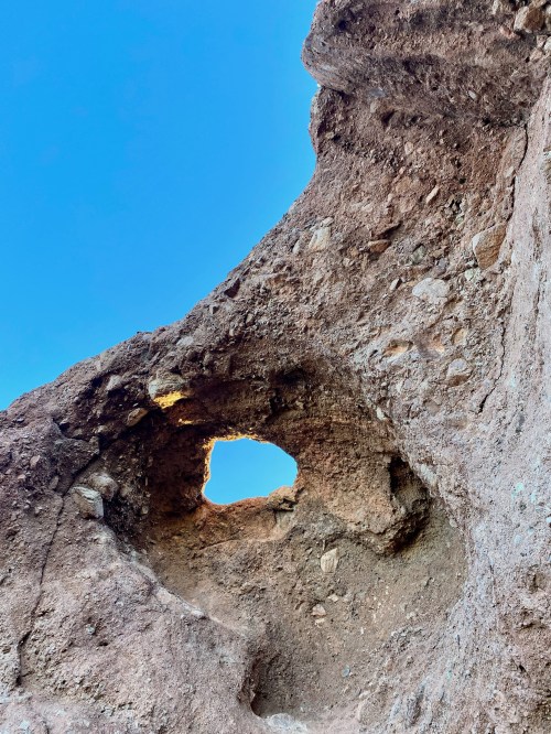 A rocky formation with a small, circular hole against a clear blue sky.