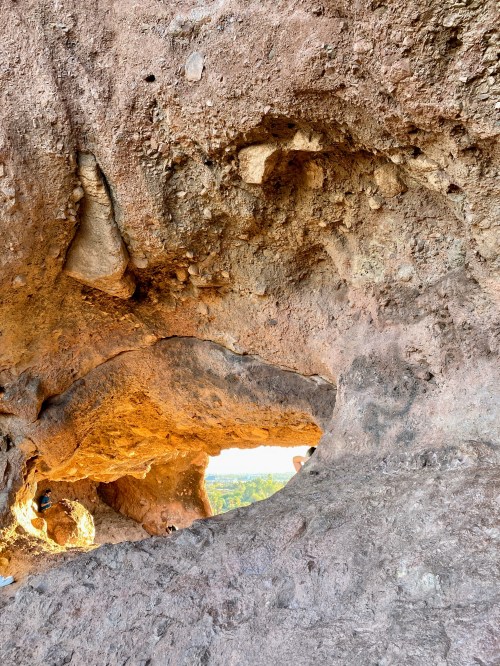 A rocky cave opening with a view of the landscape beyond, showcasing textured stone walls and natural formations.