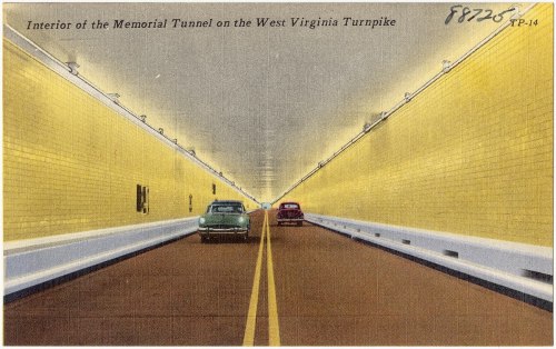 Interior of the Memorial Tunnel on the West Virginia Turnpike, featuring two cars driving through a brightly lit tunnel.