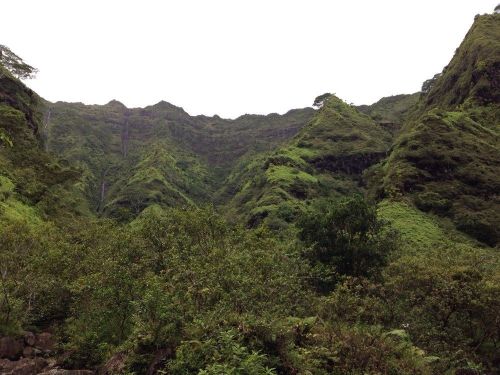 Lush green mountains rise steeply, surrounded by dense vegetation under a cloudy sky.