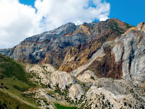 A rugged mountain landscape with colorful rock layers under a blue sky with scattered clouds.
