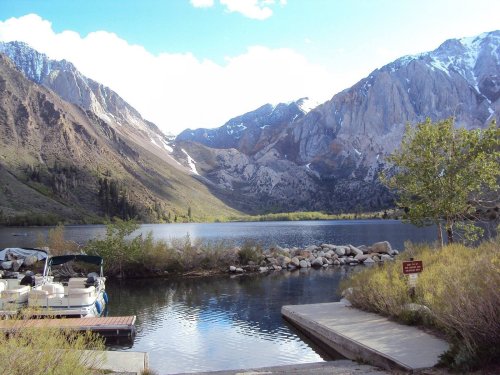 Scenic view of a lake surrounded by mountains, with a dock and a boat in the foreground under a clear blue sky.