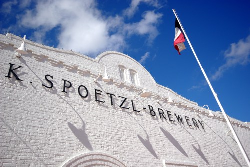 Exterior of K. Spoetzl Brewery with a Texas flag against a blue sky and white clouds.