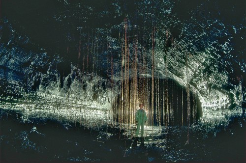 A person stands in a dark cave illuminated by glowing mineral formations hanging from the ceiling.