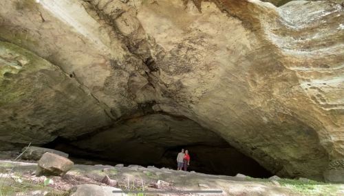 A person stands at the entrance of a large cave, surrounded by rocky terrain and towering stone walls.