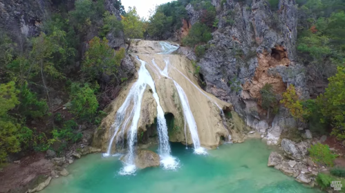 A scenic waterfall cascading over rocky cliffs into a turquoise pool, surrounded by lush greenery.