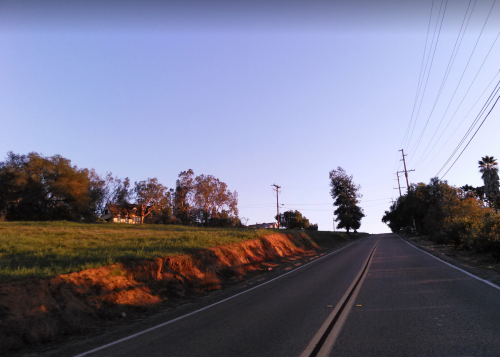 A winding road leads uphill, flanked by trees and a grassy area under a clear blue sky.
