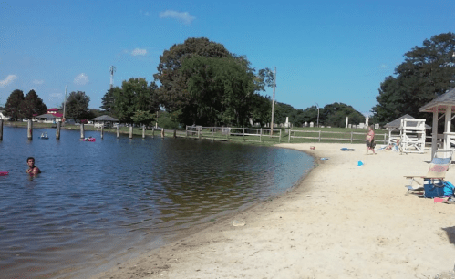 A sandy beach by a calm lake with people swimming and relaxing under a clear blue sky.