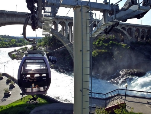 A scenic view of a cable car above a river, with a bridge in the background and lush greenery surrounding the area.