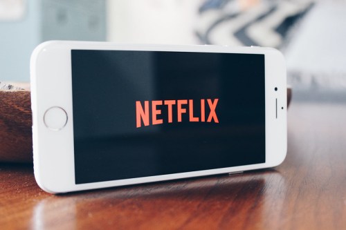 A smartphone displaying the Netflix logo on its screen, resting on a wooden surface.