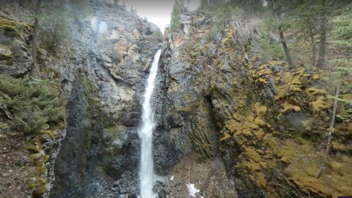 A waterfall cascading down a rocky cliff surrounded by greenery and moss.