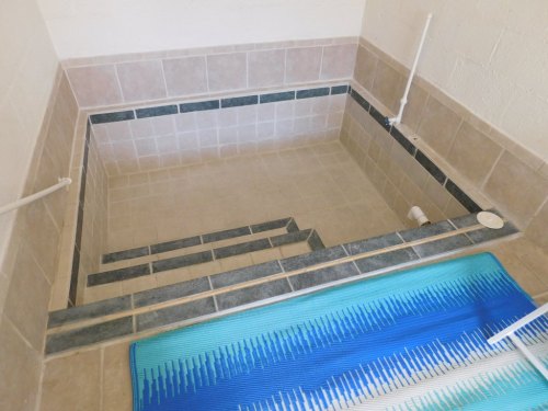 A tiled indoor pool area with steps leading down, featuring a blue and white mat on the floor.