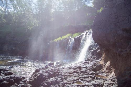 A serene waterfall cascading over rocky terrain, surrounded by lush greenery and mist in the sunlight.