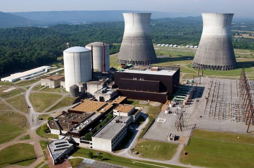 Aerial view of a nuclear power plant with cooling towers, storage tanks, and surrounding green landscape.