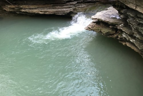 A serene body of water with a rocky edge, where a small splash occurs near the shore.