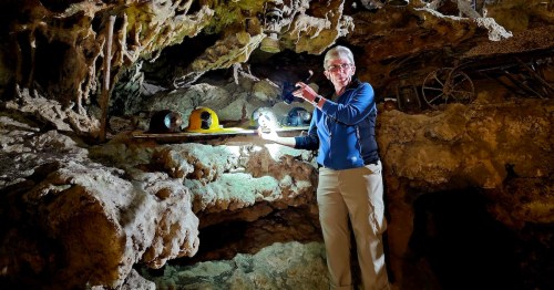 A person stands in a cave, holding a flashlight and pointing at mining equipment on a rocky ledge.