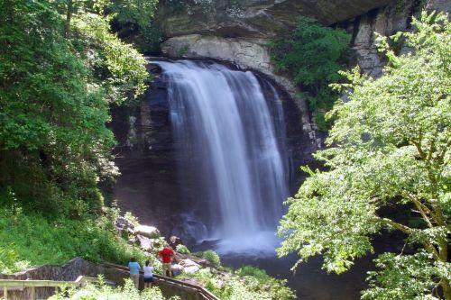 A serene waterfall cascades down rocky cliffs, surrounded by lush greenery and visitors admiring the view.