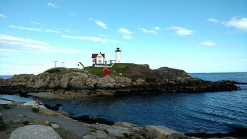 A scenic lighthouse on a rocky island, surrounded by calm blue waters and a clear sky.