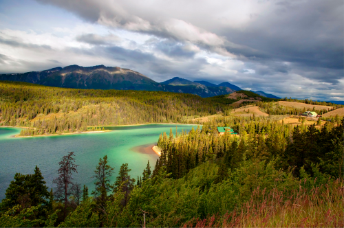 A scenic view of a lake surrounded by lush forests and mountains under a cloudy sky.