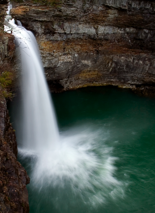 A cascading waterfall flows into a deep turquoise pool, surrounded by rocky cliffs and greenery.