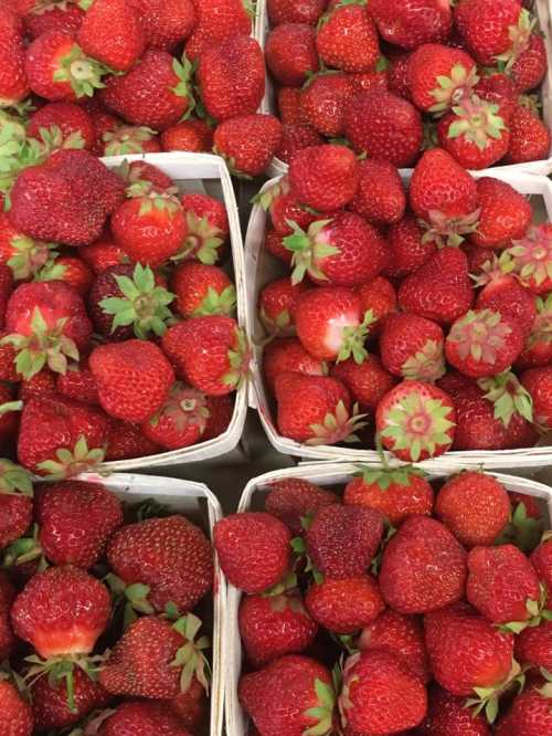 Fresh, vibrant red strawberries piled in small containers, showcasing their green leaves and juicy texture.