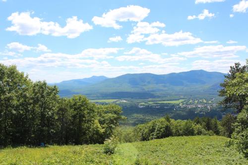 A scenic view of rolling green hills and mountains under a bright blue sky with fluffy white clouds.