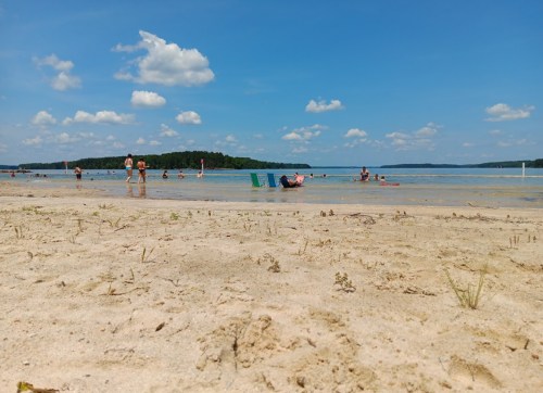 A sandy beach with people relaxing and swimming in the water under a blue sky with fluffy clouds.
