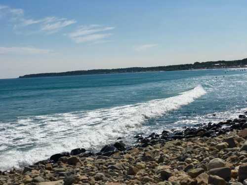 A serene beach scene with gentle waves lapping against rocky shore under a clear blue sky.