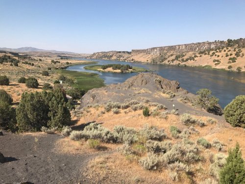 A scenic view of a river winding through arid hills and greenery under a clear blue sky.