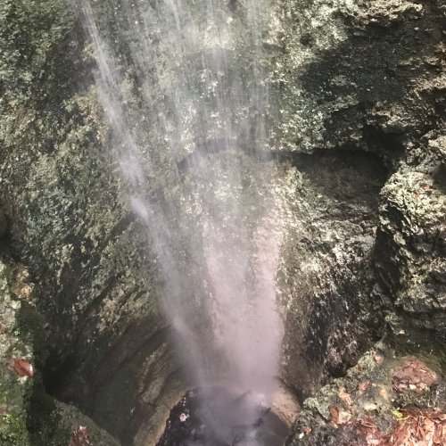 A waterfall cascading over rocky terrain, surrounded by lush greenery and mist rising from the water.