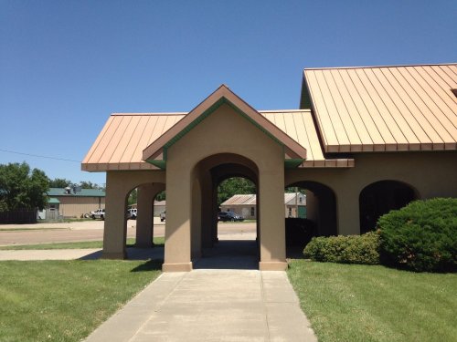 A building entrance with a brown metal roof and archway, surrounded by green grass and clear blue sky.