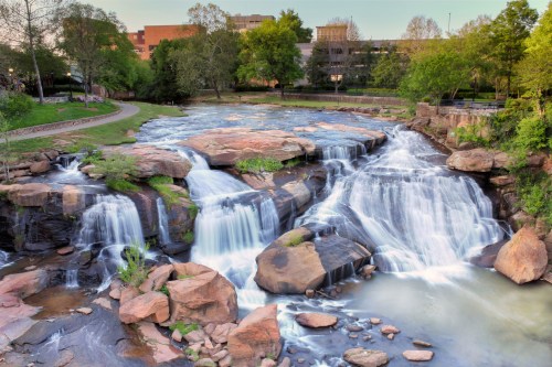 A serene waterfall cascades over rocky formations, surrounded by lush greenery and a peaceful park setting.