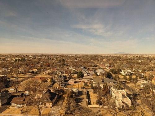 A panoramic view of a suburban landscape with houses, trees, and distant mountains under a clear blue sky.