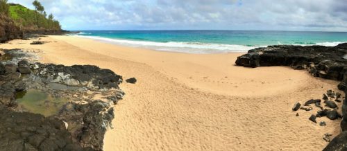 A serene beach scene with golden sand, rocky formations, and calm turquoise waters under a cloudy sky.