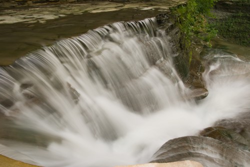 A serene waterfall cascading over rocks, surrounded by lush greenery and smooth water flow.