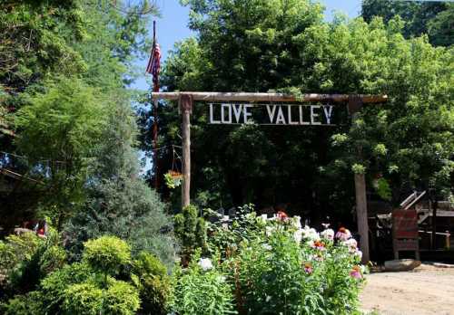 A wooden sign reading "Love Valley" surrounded by lush greenery and colorful flowers in a scenic outdoor setting.