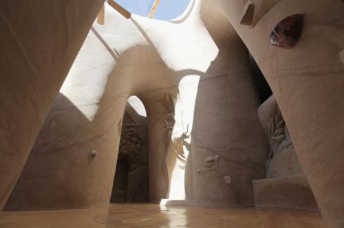 Interior of a sculptural space with curved walls, natural light streaming in, and artistic textures.
