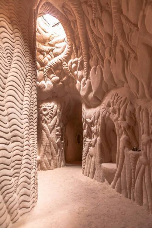 A textured, sandy corridor with intricate, organic patterns on the walls, illuminated by soft, natural light.